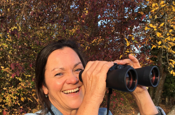 Foto einer lachenden Frau mit Fernglas in der Hand