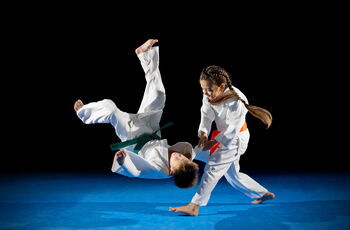 Foto von zwei kämfenden Kindern (Junge und Mädchen) im weißen Karateanzug. Der Junge wird gerade zu Boden geworfen.