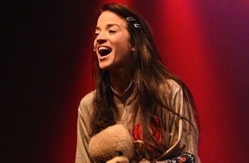 Foto eines lachenden Mädchens mit langen braunen Haaren und Teddy im Arm