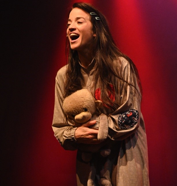 Foto eines lachenden Mädchens mit langen braunen Haaren und Teddy im Arm